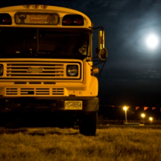 A bus, turned camper van, is light up by the full moon - Destination Sasquatch!. Photo by Kim Jay.
